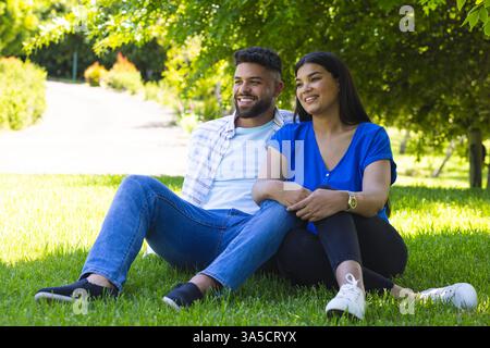 Paare sitzen auf Gras im Park, lächeln und genießen den sonnigen Tag zusammen Stockfoto