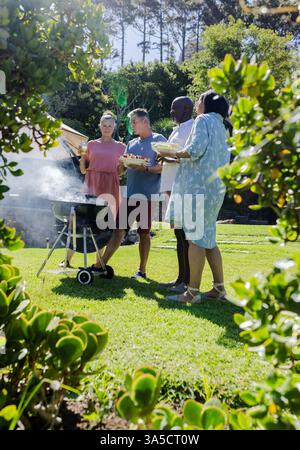 Ältere Freunde genießen im sonnigen Hinterhof Barbecue im Freien, plaudern und servieren Speisen Stockfoto
