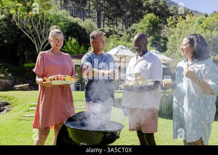 Grillen und Lachen, Seniorenfreunde grillen im sonnigen Hinterhof Stockfoto