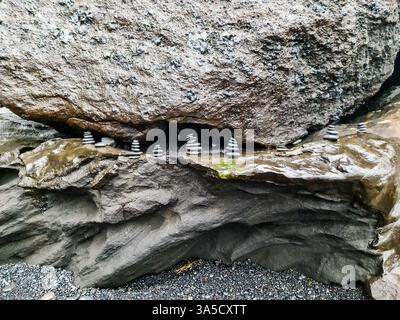 Kleine steinhügel aus ausgleichenden Steinen, die auf nassen Felsen unter einem großen Felsbrocken stehen und eine friedliche und meditative Atmosphäre schaffen Stockfoto