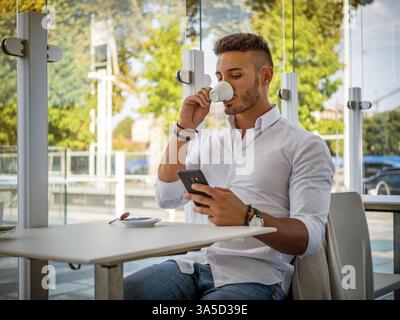 Nahaufnahme von gutaussehenden jungen Mann Kaffee trinken im Shop bei Handy suchen Stockfoto