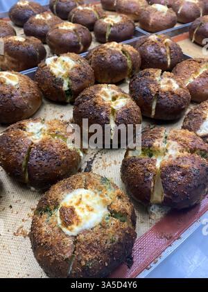 Frisch gebackene Brötchen mit goldener Kruste und geschmolzenem Käse kühlen in einer lebhaften Bäckereiküche ab und füllen die Luft mit einem herrlichen Aroma. Stockfoto