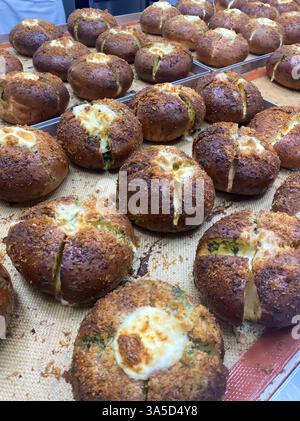 Frisch gebackene Brötchen mit goldener Kruste und geschmolzenem Käse kühlen in einer lebhaften Bäckereiküche ab und füllen die Luft mit einem herrlichen Aroma. Stockfoto