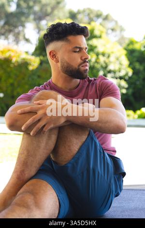 Mann, der sich draußen entspannt, auf Yogamatte sitzt, friedliche Momente im Garten genießt Stockfoto