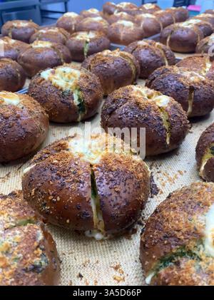 Frisch gebackene Brötchen mit goldener Kruste und geschmolzenem Käse kühlen in einer lebhaften Bäckereiküche ab und füllen die Luft mit einem herrlichen Aroma. Stockfoto