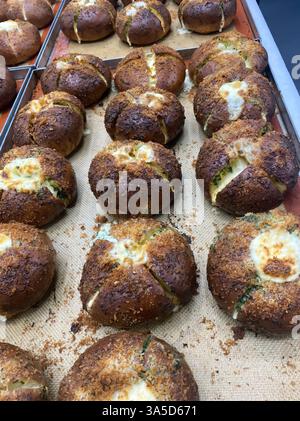 Frisch gebackene Brötchen mit goldener Kruste und geschmolzenem Käse kühlen in einer lebhaften Bäckereiküche ab und füllen die Luft mit einem herrlichen Aroma. Stockfoto