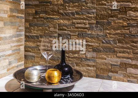Stillleben mit einer schwarzen Glaskanne, einem transparenten Glas und zwei Kerzenleuchtern. Steinmauer im Hintergrund. Das Konzept der künstlerischen Fotografie Stockfoto
