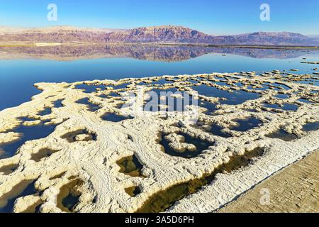 Verdampftes Salz bildet bizarre Muster auf dem Wasser. Totes Meer. Das blaue Wasser ist von rosa Bergen umgeben. Sonniger Wintertag. Das Foto wurde aufgenommen Stockfoto