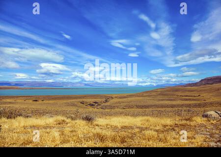 Das Konzept des aktiven und exotischen Tourismus. Flache Ebene mit flachem See und gelblichem Gras. Patagonische Pampas. Starker Wind trägt Wolken Stockfoto