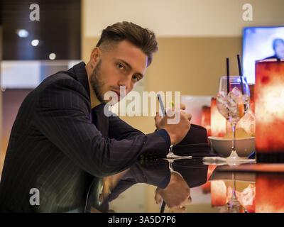 Hübscher junger Mann trinken Cocktail an der Theke, trägt Anzug und Kamera Stockfoto
