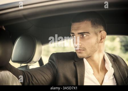 Hübscher junger Mann, der ein Auto fährt, trägt schwarze Jacke, die Hand auf das Rad Stockfoto