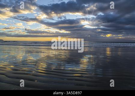 Leichter Wind verursacht kleine Wellen im Wasser. Neuseeland, Pazifikküste. Morgens Ruhig. Sanfte Wolkenfarben spiegeln sich im Meereswasser wider. Konz Stockfoto