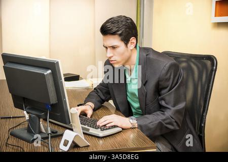 Schwere hübscher junger Geschäftsmann sitzt an seinem Schreibtisch im Büro am Computer arbeiten Stockfoto