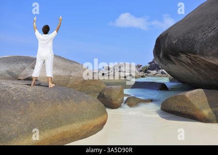 Thailand. Wunderschöner Strand auf den Similan Inseln. Frau mittleren Alters, weiß gekleidet, beim Yoga. Posiere den Segen der Sonne Stockfoto