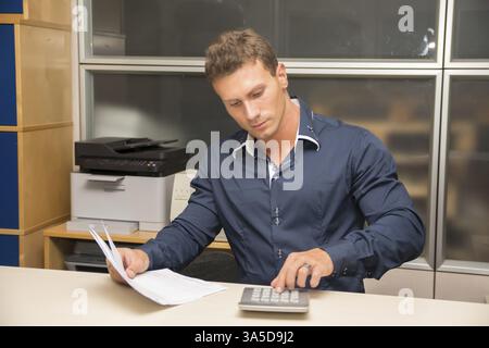 Hübscher junger Mann arbeiten im Büro am Schreibtisch mit Taschenrechner Stockfoto