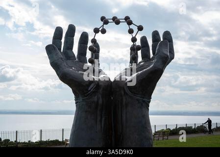 Ramsgate, Großbritannien. März 2025. Ein Mann schiebt sein Fahrrad an den Händen und Molekülskulptur auf der Westcliff Promenade in Ramsgate. Die Hand- und Molekülskulptur stammt von David Barnes. Laut David Barnes ist dies „eine Anspielung auf die Entdeckung, Entwicklung und Herstellung innovativer Arzneimittel“ in Kent. Die 1,8 m hohe Bronzestatue wurde vom Pharmagiganten Pfizer gegründet. Das Kunstwerk befindet sich auf der Westcliff Promenade in Ramsgate. Quelle: SOPA Images Limited/Alamy Live News Stockfoto