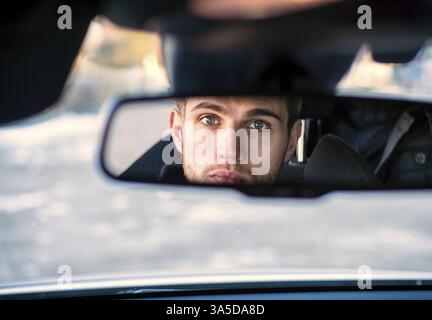 Schönen blonden jungen Mann, der ein Auto fährt, mit schwarzen Pullover. Hand auf Rad Stockfoto