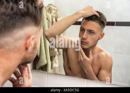 Gut aussehender Mann Blick auf sein Gesicht im Spiegel, Überprüfung von Haar und Haaransatz Stockfoto