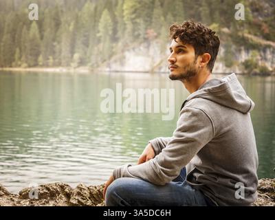 Schöner Yung-Mann, der auf dem Hintergrund des Waldes am Ufer des Sees steht und wegblickt Stockfoto