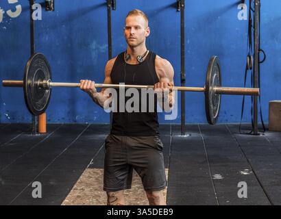 Gutaussehender muskulöser junger Mann, der Arme im Fitnessstudio mit Langhantel trainiert Stockfoto