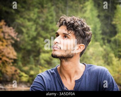 Schöner Yung-Mann, der auf dem Hintergrund des Waldes steht und wegblickt Stockfoto