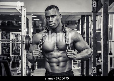Attraktive Hunky schwarzen männlichen Bodybuilder Bodybuilding Pose im Fitness-Studio mit Eisenketten über Schultern zu tun Stockfoto