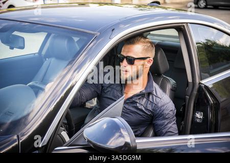 Porträt des jungen bärtigen Mann mit Sonnenbrille immer aus seinem neuen stilvollen polierten Auto im freien Stockfoto