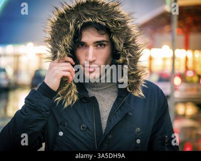 Volle Länge des jungen Mannes im Fell Wandern unter Regen entlang der Straße der Stadt Stockfoto