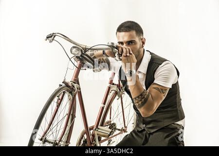 Porträt eines jungen tätowierten Mannes in eleganten Kleidern und Schuhen, der Fahrrad fährt. Isolate. Studio-Aufnahme Stockfoto