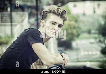 Profilaufnahme eines attraktiven, blonden jungen Mannes in der Stadt, der draußen in die Kamera schaut Stockfoto