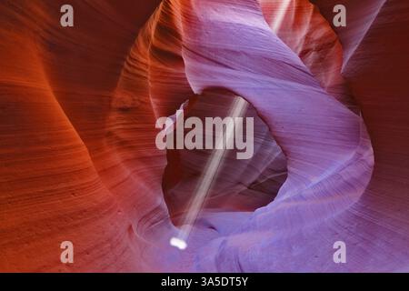 Mittag in einem rot-Orange Antelope Canyon. Ein dünner Strahl des Tageslichtes leuchtet auf dem sandigen Boden des Canyons Stockfoto