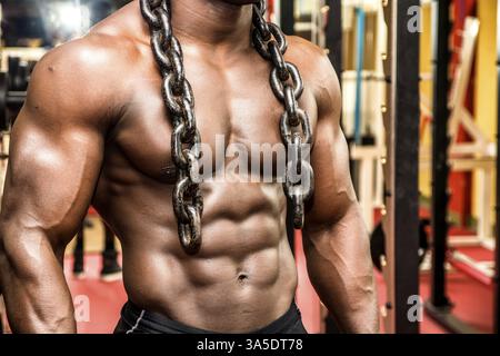 Attraktive Hunky schwarzen männlichen Bodybuilder Bodybuilding Pose im Fitness-Studio mit Eisenketten über Schultern zu tun Stockfoto