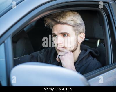 Schönen blonden jungen Mann, der ein Auto fährt, mit schwarzen Pullover. Hand auf Rad Stockfoto