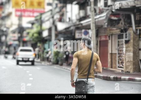 Rückansicht eines jungen, fitten Mannes, der auf einer belebten sonnigen Straße in Bangkok, Thailand, Asien spaziert Stockfoto