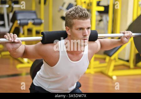 Hübscher junger Mann macht Kniebeugen im Fitness-Studio mit Langhantel Stockfoto