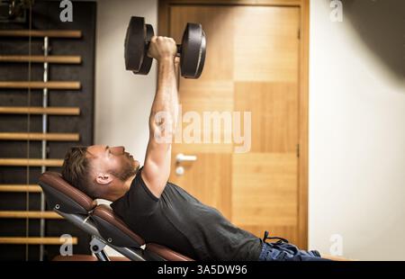 Muskulöser junger Mann, der Hanteln hebt und Pecs auf der Turnbank trainiert Stockfoto