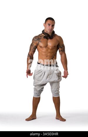 Porträt des muskulösen Mannes mit rasiertem Kopf stehend im Studio mit weißem Hintergrund, der weiße Hosen und kleine Boa- oder Python-Schlangenpackung trägt Stockfoto