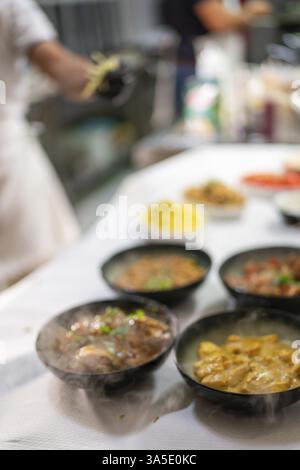 Eine Küchenszene mit mehreren Schüsseln mit zubereiteten Gerichten, ein Koch arbeitet im Hintergrund Stockfoto