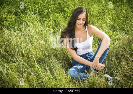 Porträt der Schönen lächelnde Mädchen mit langen Haaren sitzen auf grünem Gras und Suchen nach unten Stockfoto