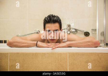 Hübscher junger Mann in Badewanne zu Hause Bad, stützte sich auf Wannenrand, Blick in die Kamera Stockfoto