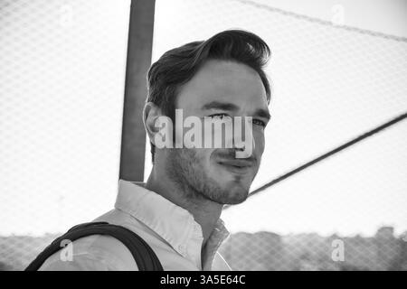 Hübscher junger Mann zu Fuß in die Stadt mit Rucksack auf der Schulter, trägt weißes Hemd, Blick in die Kamera Stockfoto