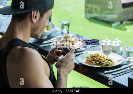 Seitenansicht eines hübschen jungen Mannes, der ein Foto von seinem Essen im Restaurant macht. Horizontale Innenaufnahme Stockfoto