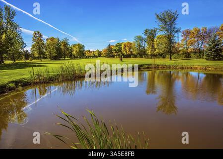 Rot-grünes Herbstlaub spiegelt sich in einem kleinen Teich mit Lehmboden wider. Strahlender sonniger Tag in Französisch-Kanada. Das Konzept des Freizeittourismus Stockfoto