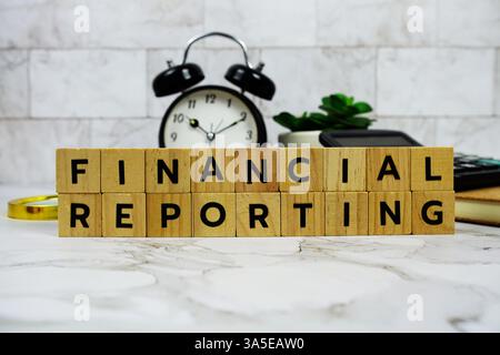 Finanzberichterstattung mit Holzblöcken Alphabetbuchstaben und Wecker auf Marmorhintergrund Stockfoto
