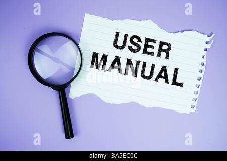 Text im Benutzerhandbuch auf Papier geschrieben mit Lupe flach auf violettem Hintergrund Stockfoto