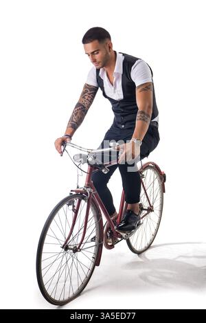 Porträt eines jungen tätowierten Mannes in eleganten Kleidern und Schuhen, der Fahrrad fährt. Isolate. Studio-Aufnahme Stockfoto