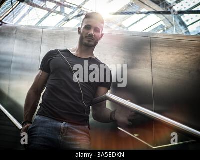Hübscher junger Mann im Bahnhof, der auf Treppen läuft und in die Kamera blickt Stockfoto