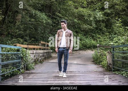 Hübscher junger Mann in einer üppigen grünen Berglandschaft wandern über eine Brücke in den Wald auf der Suche auf einer Seite Stockfoto
