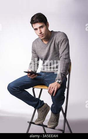 Hübscher junger Mann hält Ebook-Reader und Blick in die Kamera, sitzen auf weißem Hintergrund Stockfoto