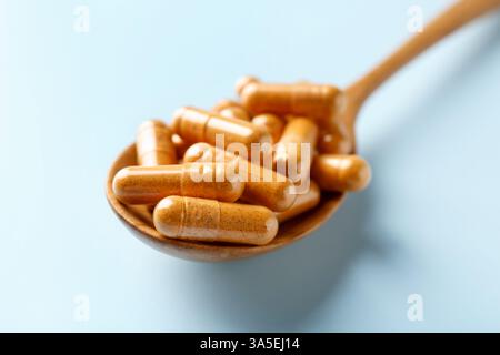Kurkuma-Kapseln im Holzlöffel auf hellblauem Hintergrund, Großaufnahme Stockfoto